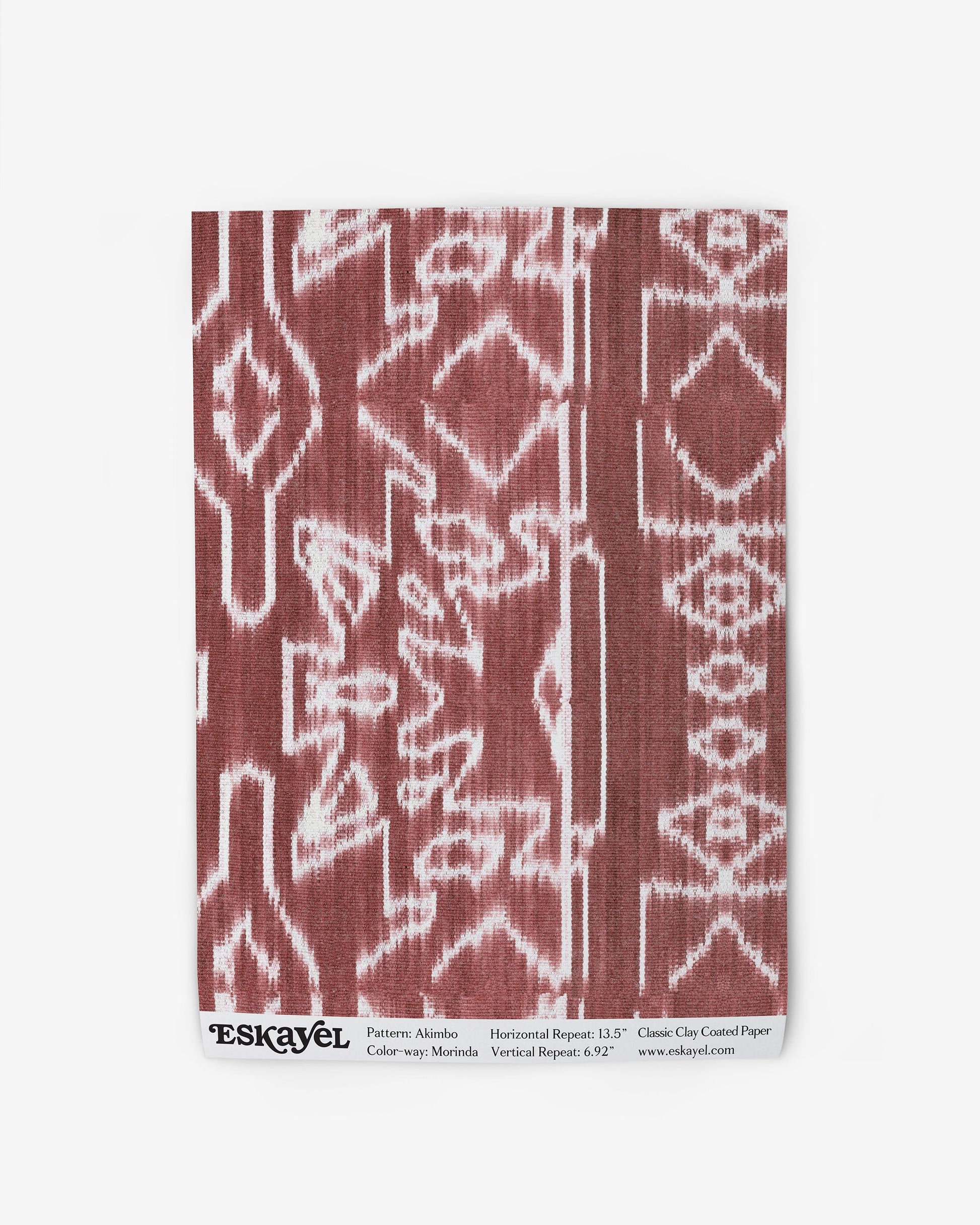 A red and white Akimbo Wallpaper Sample Morinda Ikat pattern on a piece of cloth sample