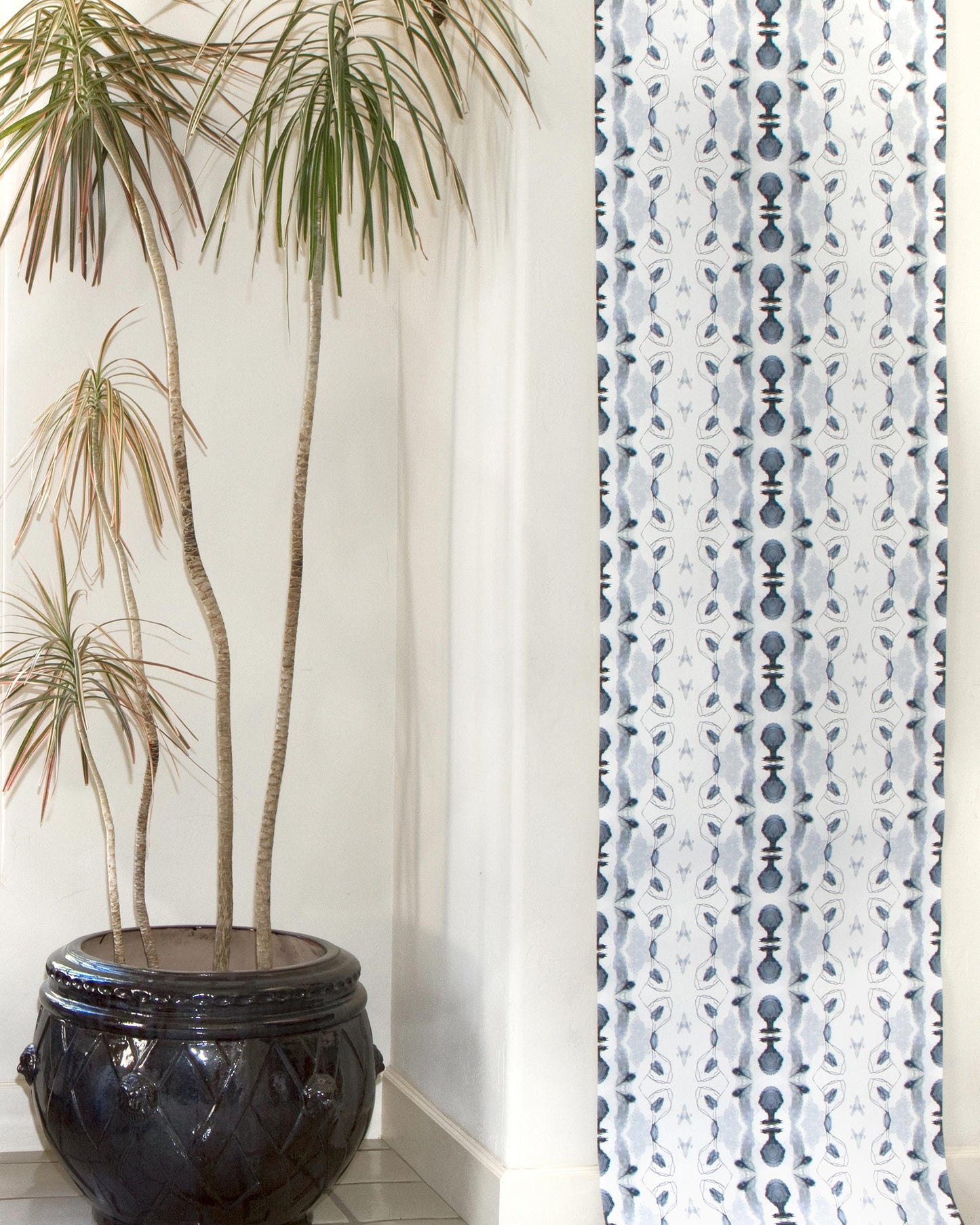 A white Bali Stripe Wallpaper Indigo wall hanging with Indigo aesthetic and a plant in front of it