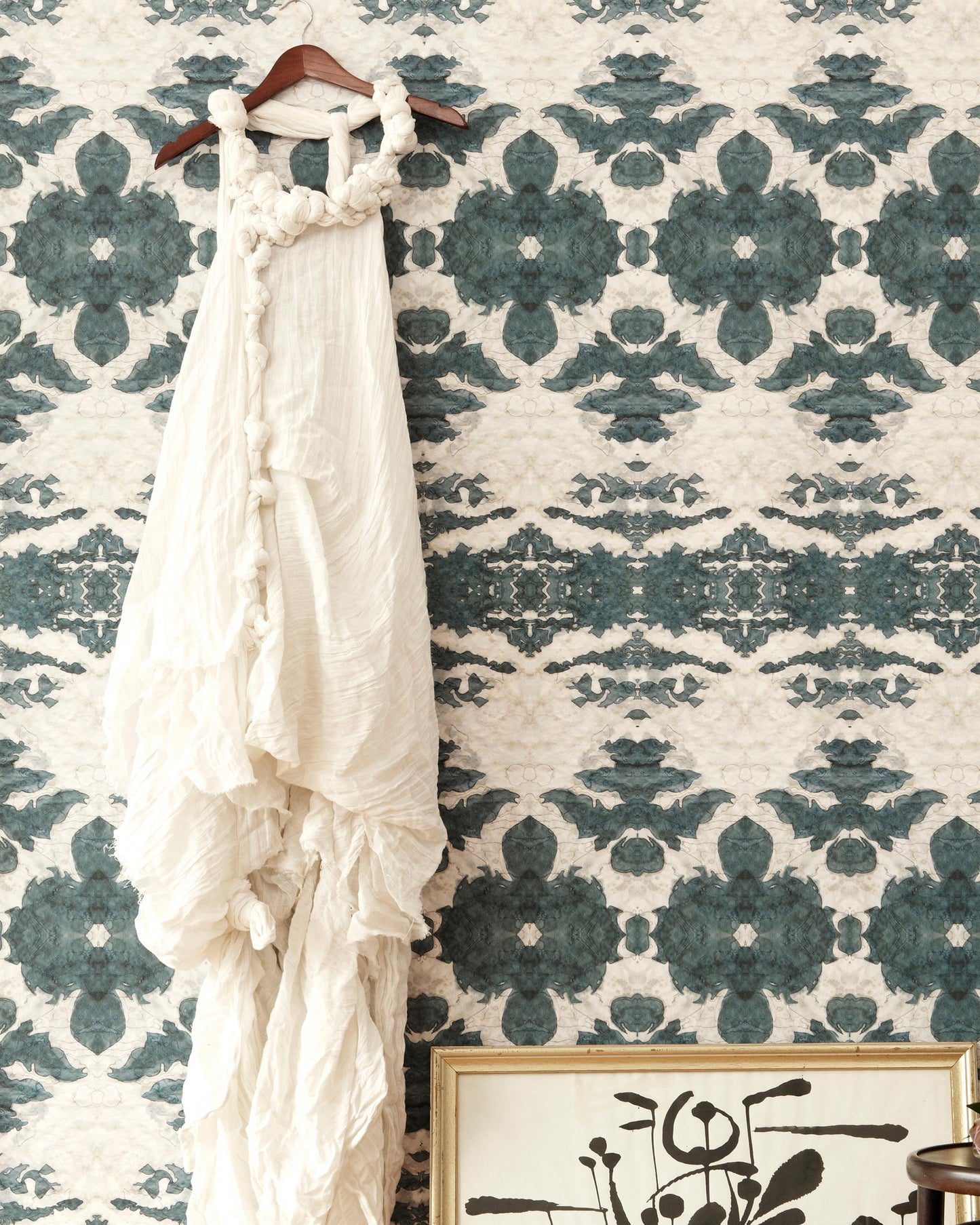 A white dress hangs on a wall in front of The Dance Wallpaper Olive
