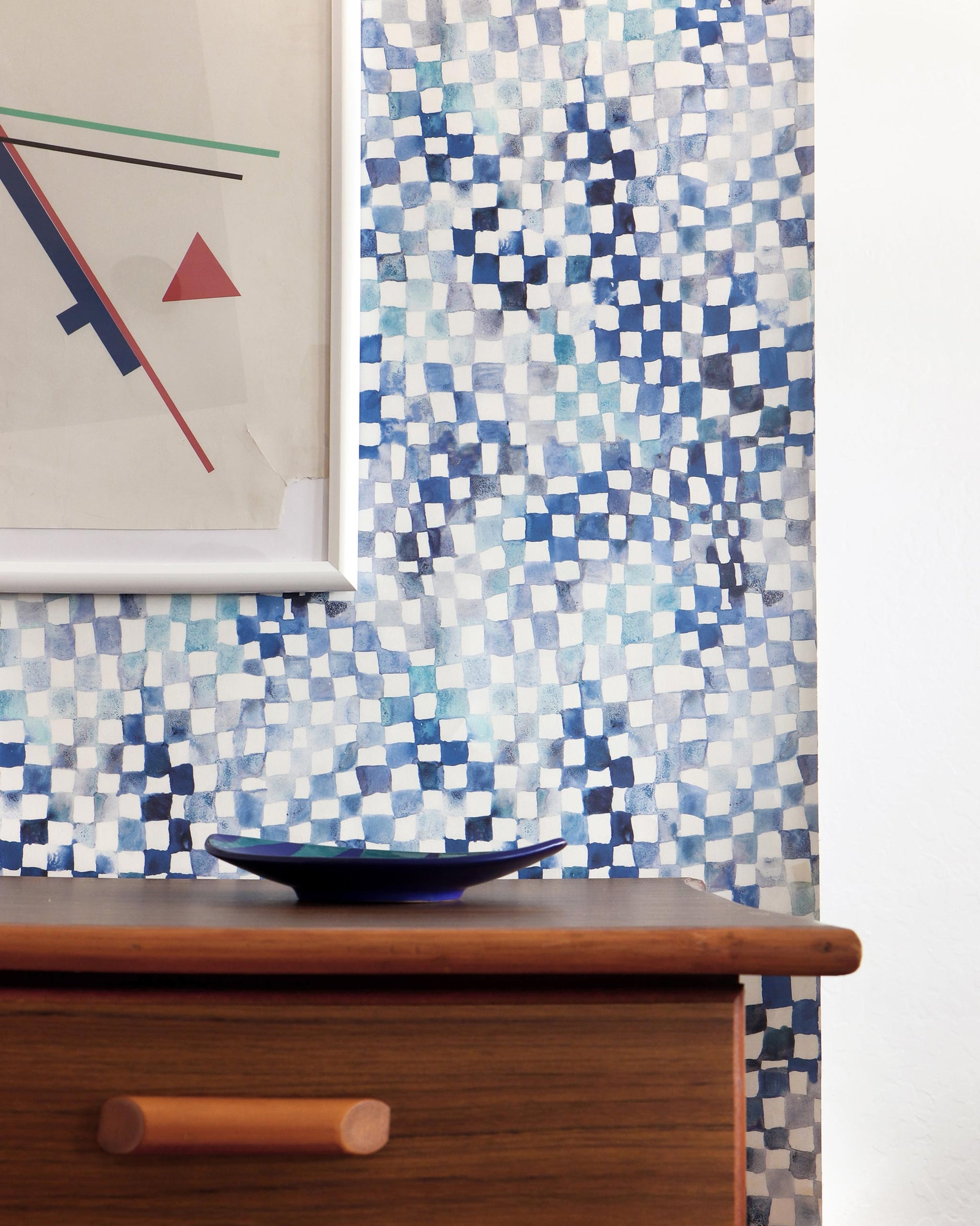 A blue and white Chess Wallpaper Ocean tiled wall behind a dresser