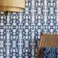 A wicker chair in front of a blue and white luxury Biami Wallpaper with the Nila pattern
