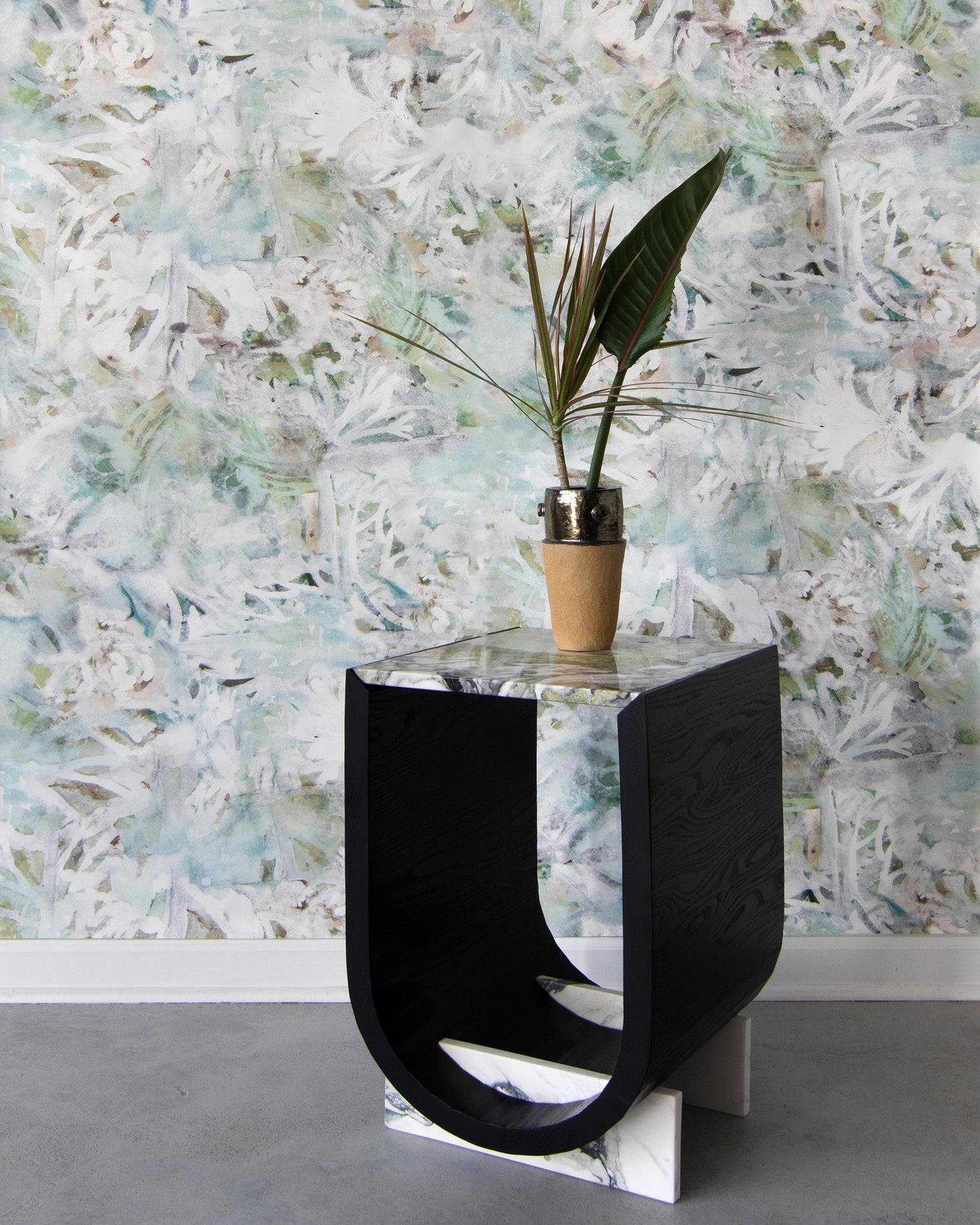 A small table with a plant on it in front of a custom Cortile Wallpaper Verde