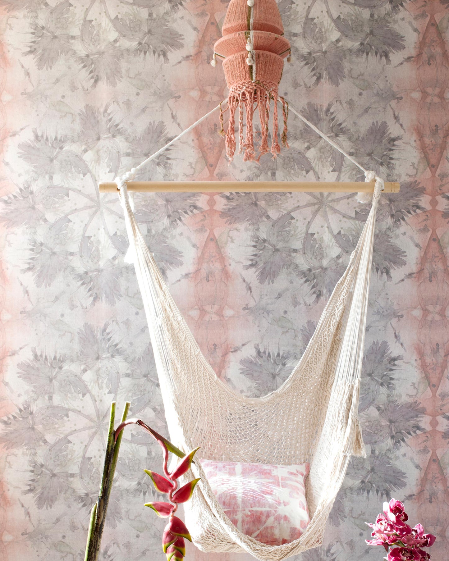 A hanging chair in a room with a pink Laurel Forest Wallpaper Persimmon wall panel
