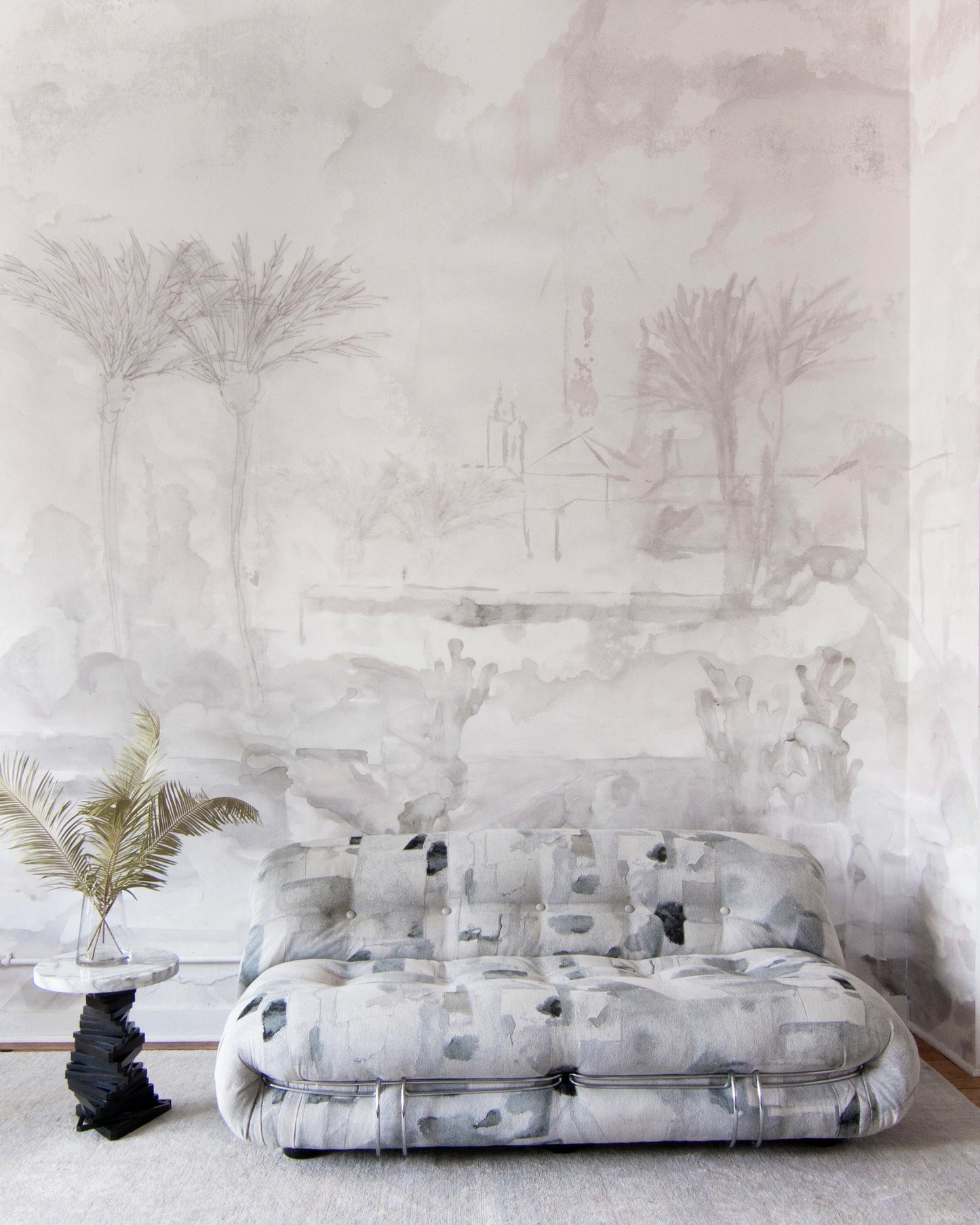 A white couch in front of a Palmeraie Wallpaper Mural with a painting of palm trees is enhanced with luxury fabric