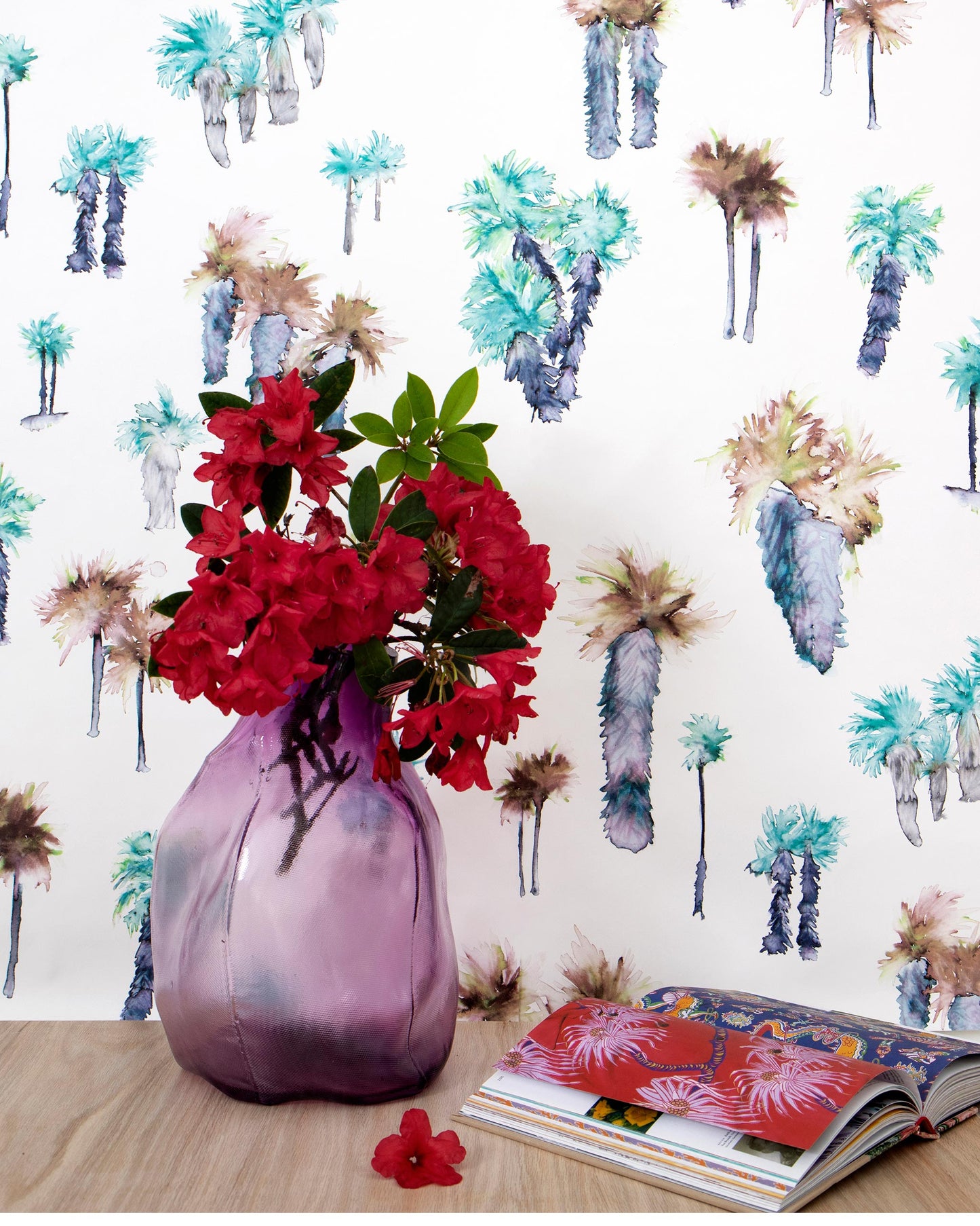 A luxury fabric tablecloth with a vase of flowers and a book on top is complemented by the presence of Perfect Palm Wallpaper Pool outside the window