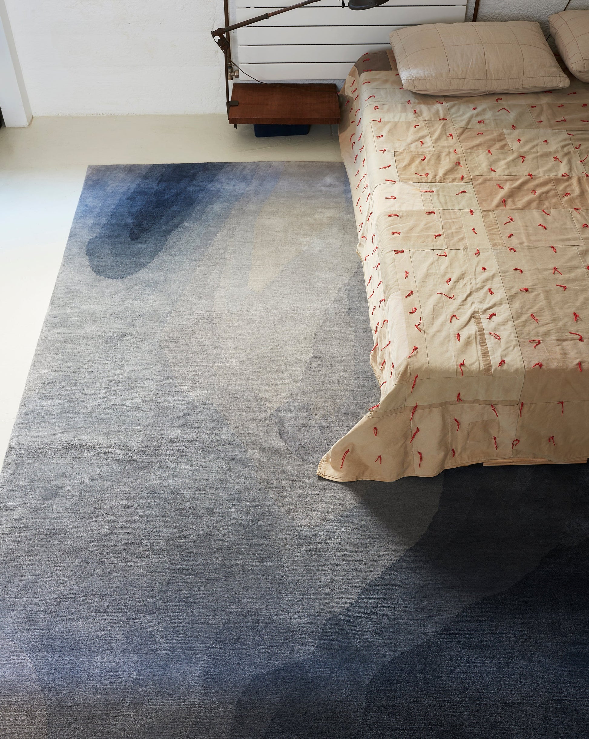 A bedroom with a bed and a Progressions Hand Knotted Rug Gulf in a Gulf colorway