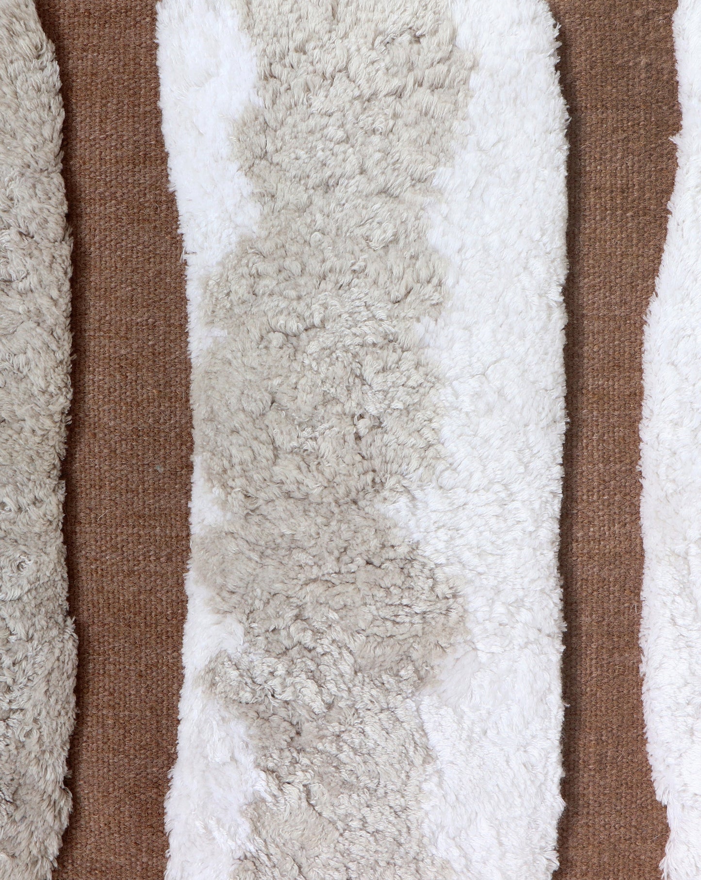 A row of Bold Stripe Hand Knotted Rug Sandstone sheepskin pillows on a brown background