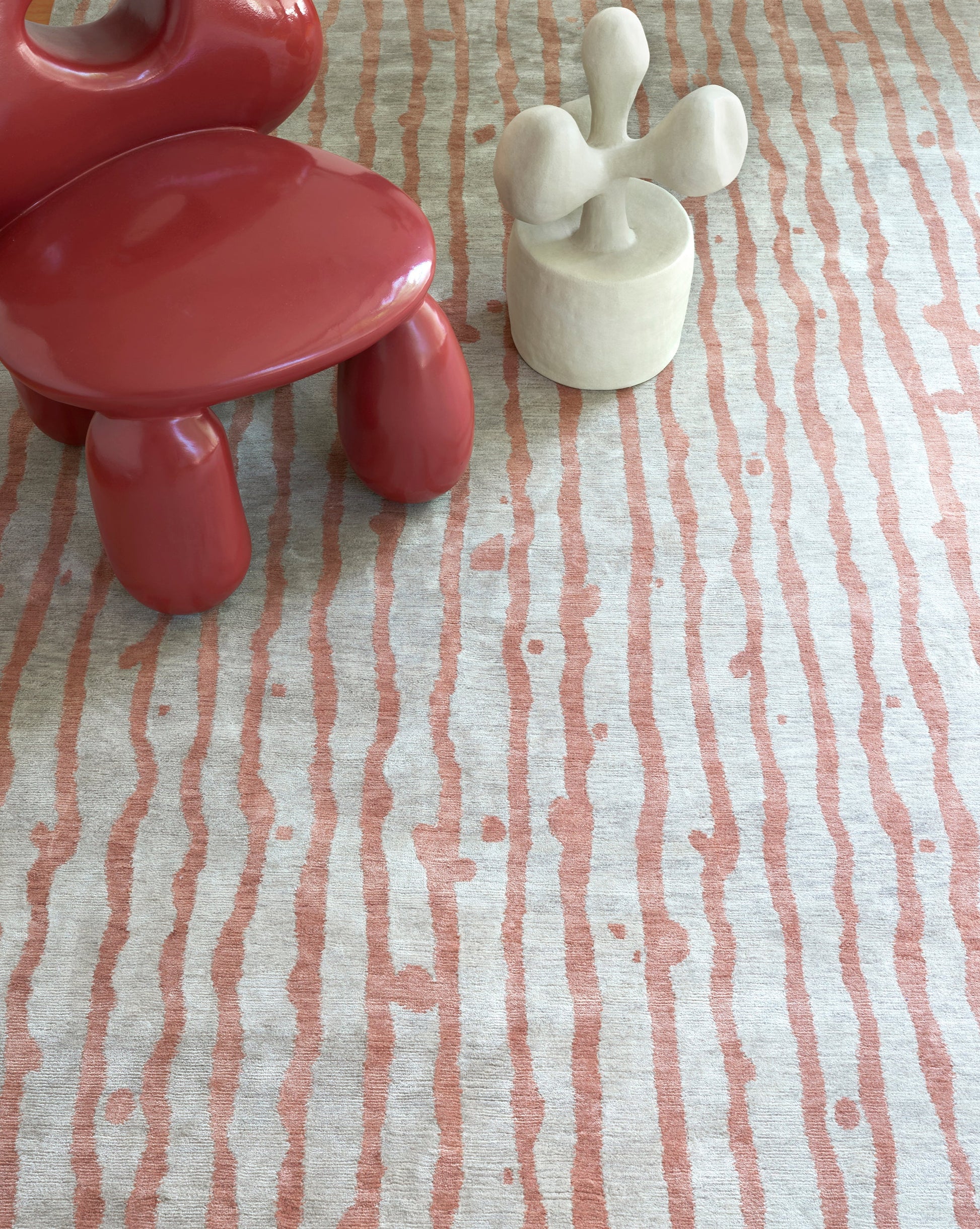 A red chair on a Drippy Stripe Hand Knotted Rug Sienna next to a cactus