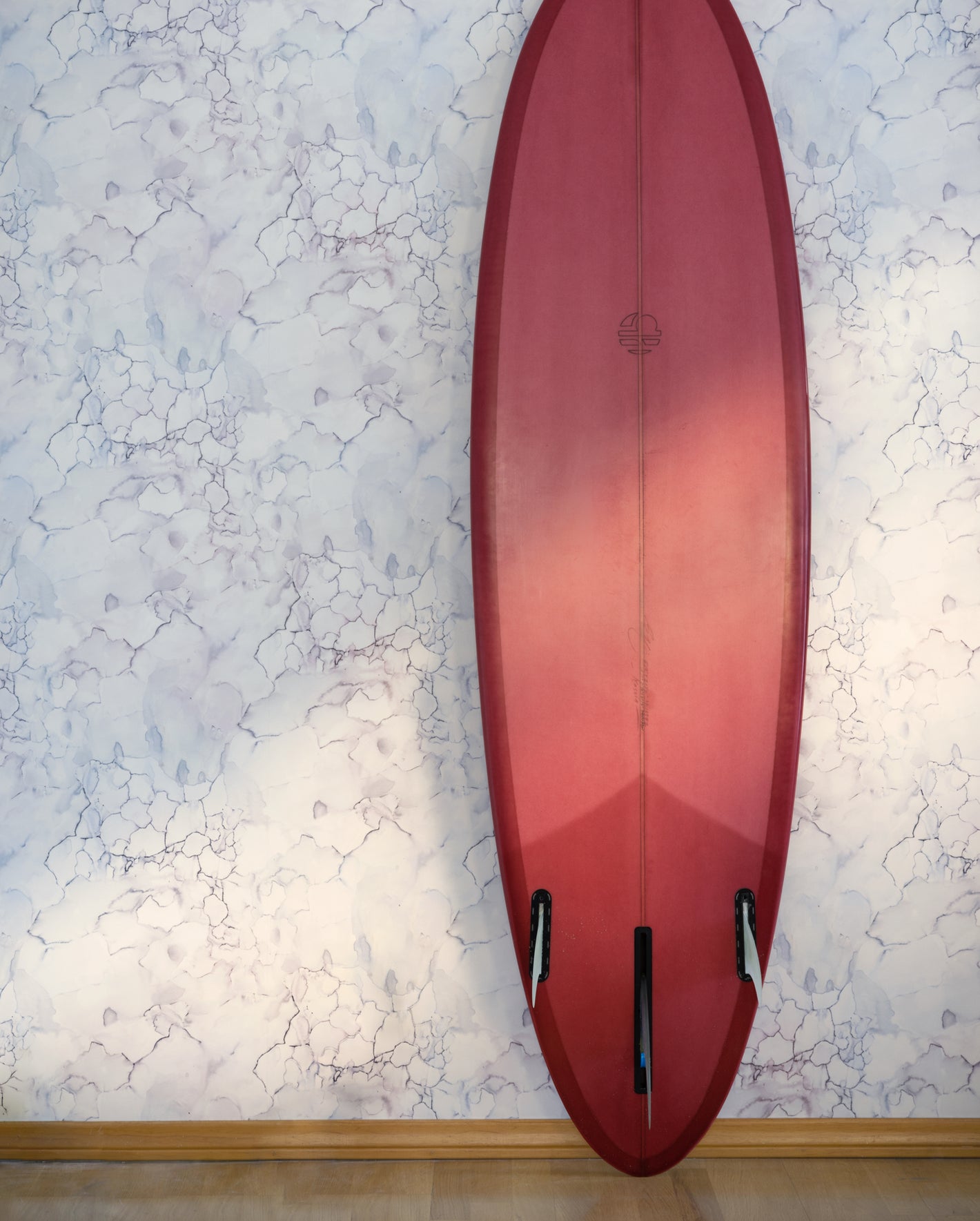 A red surfboard leans against a wall