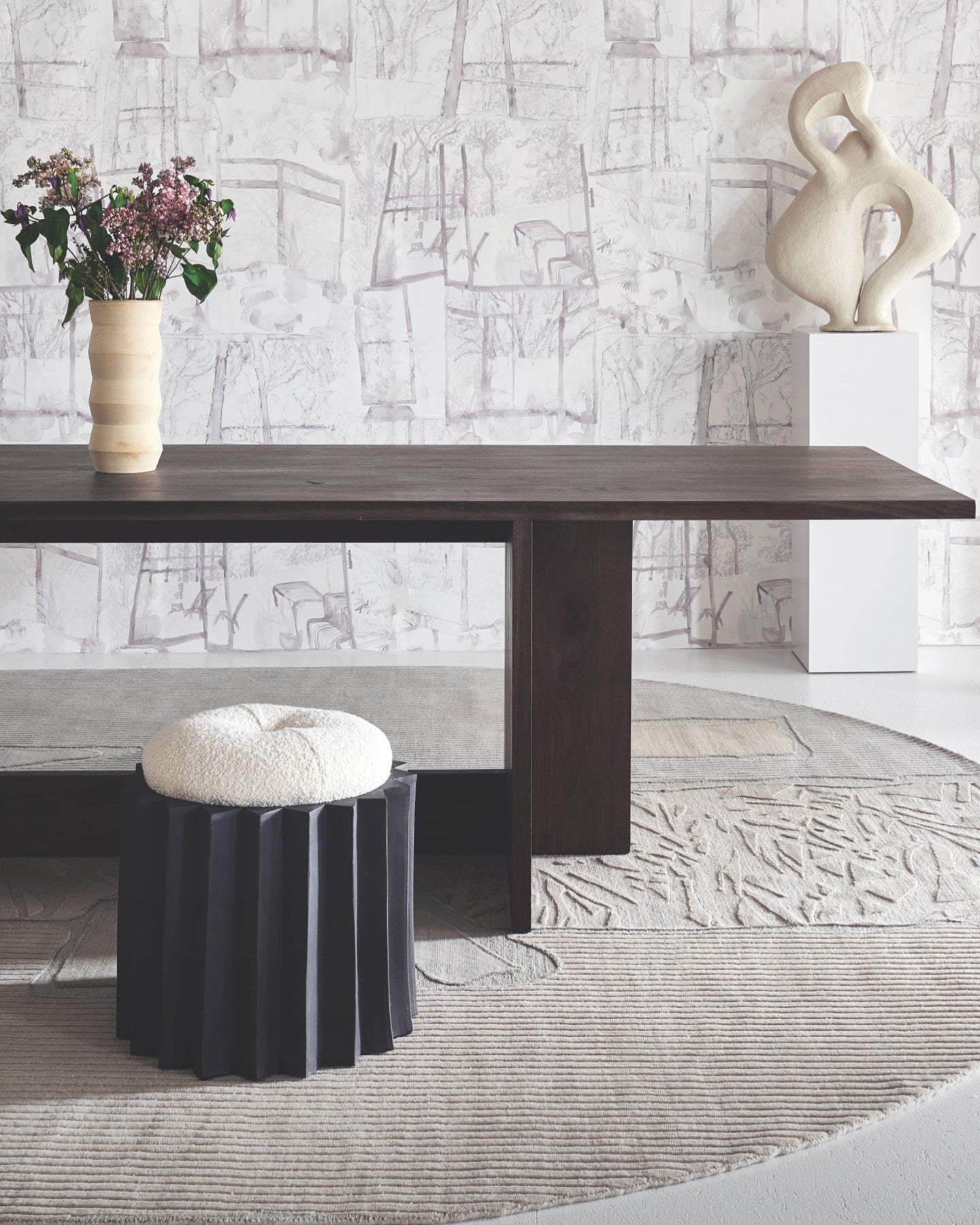 A dining table and a stool in a room with wallpaper