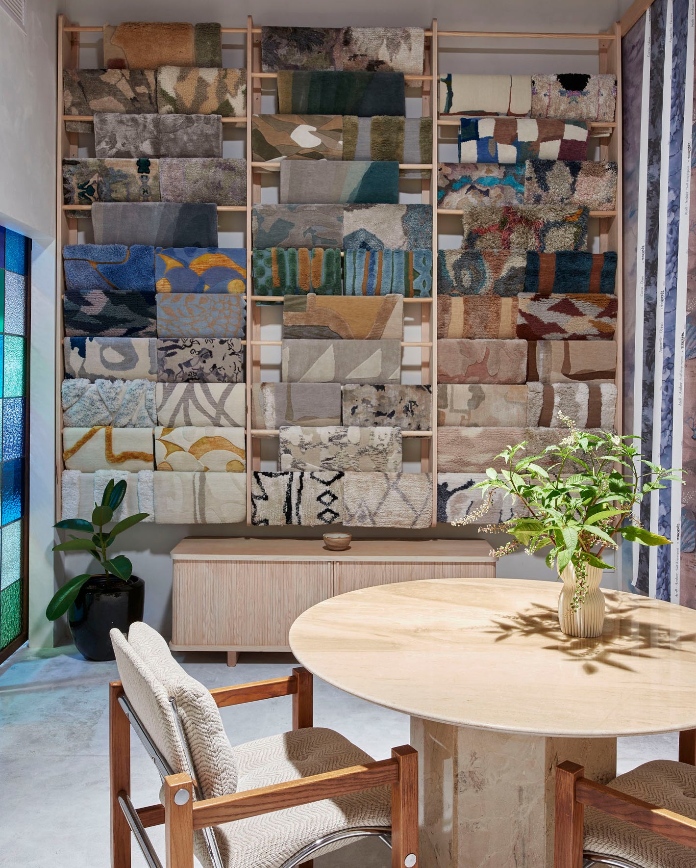 A room with a large wall display of rug samples and a round table.