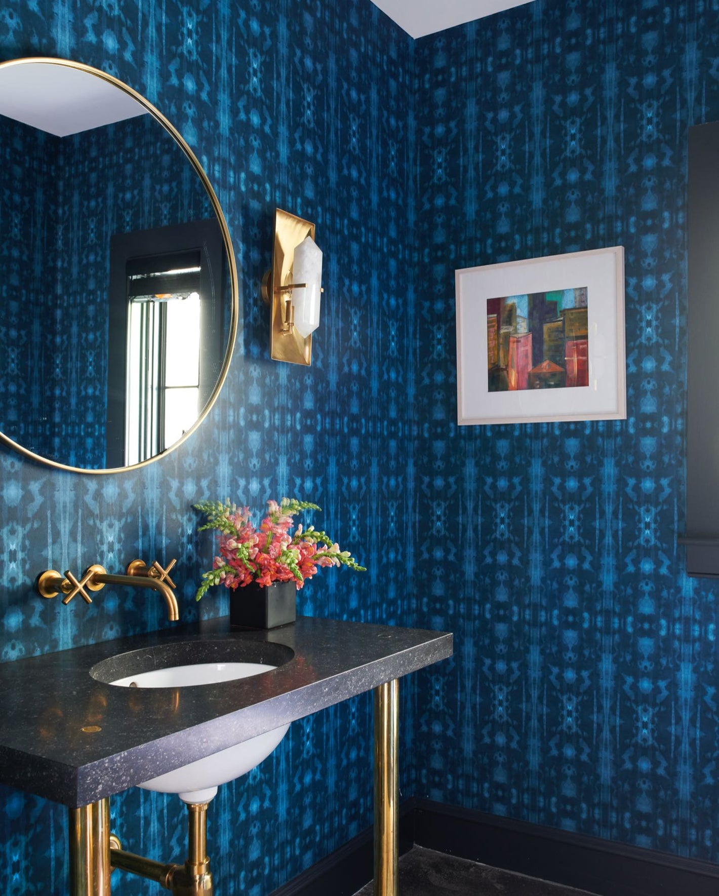 A bathroom with blue wallpaper and a gold mirror