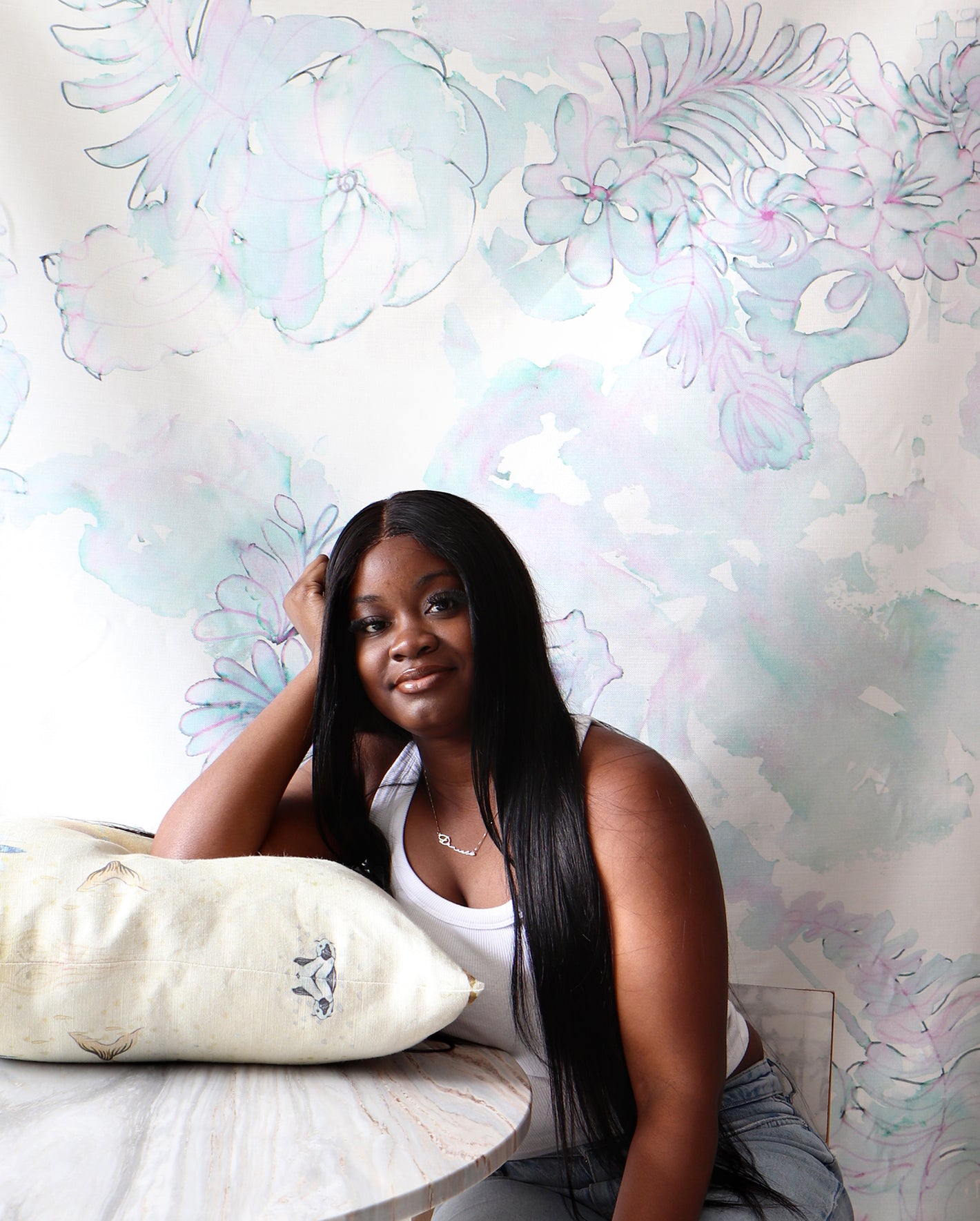 A woman posing with a pillow in front of a wall covered in a floral wallpaper..