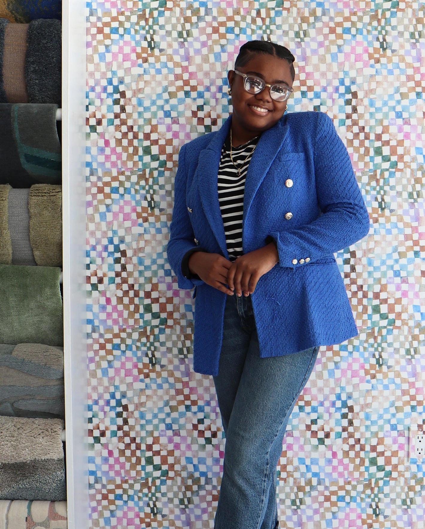 A woman in a blue blazer standing in front of a multi colored checkered wall.