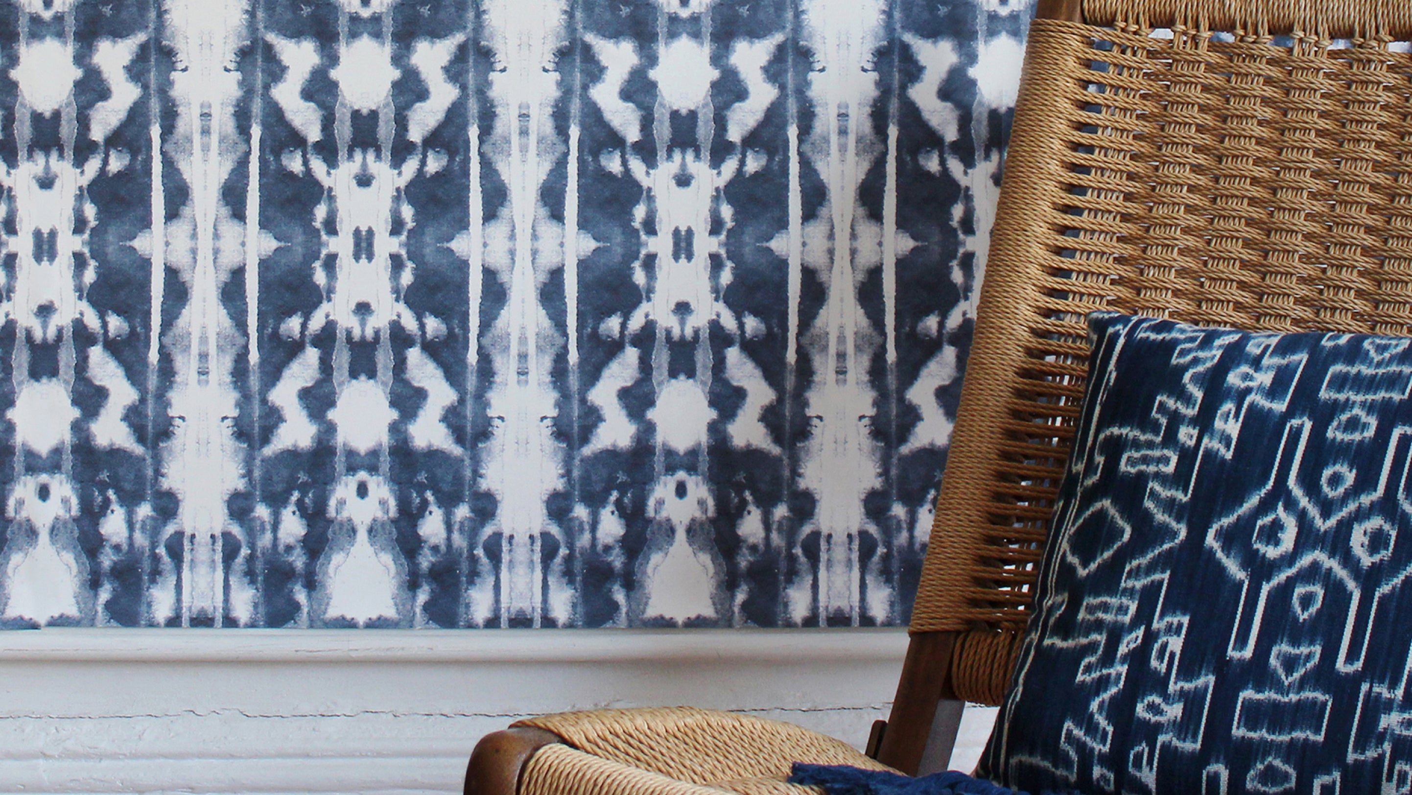 A wicker chair in front of a blue and white patterned wallpaper