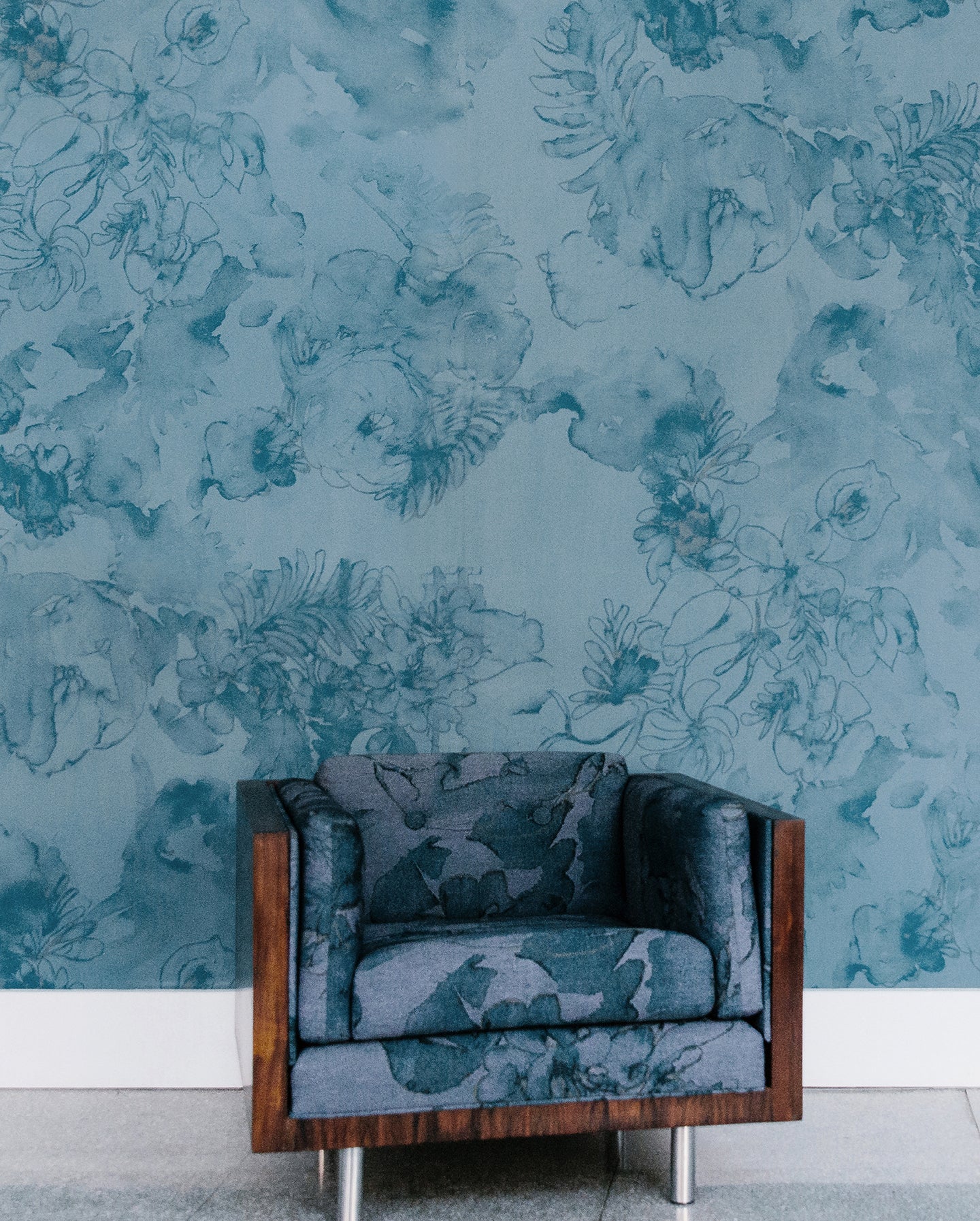 A chair in front of a blue floral wallpaper