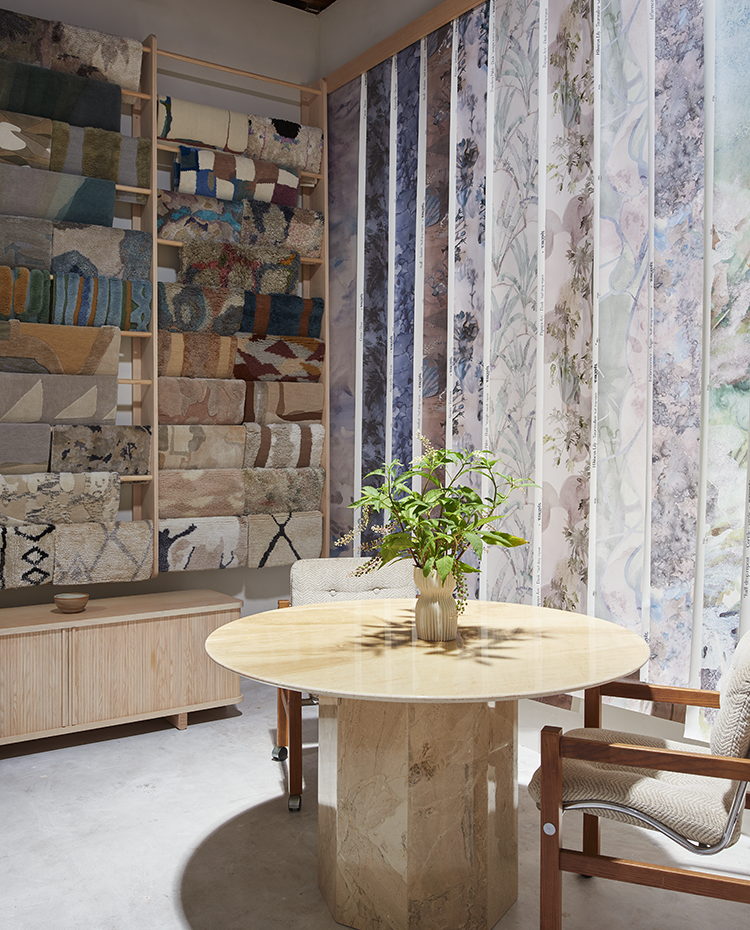 Sitting room with a round marble table, chairs, and a wall of wallpaper and rug samples.