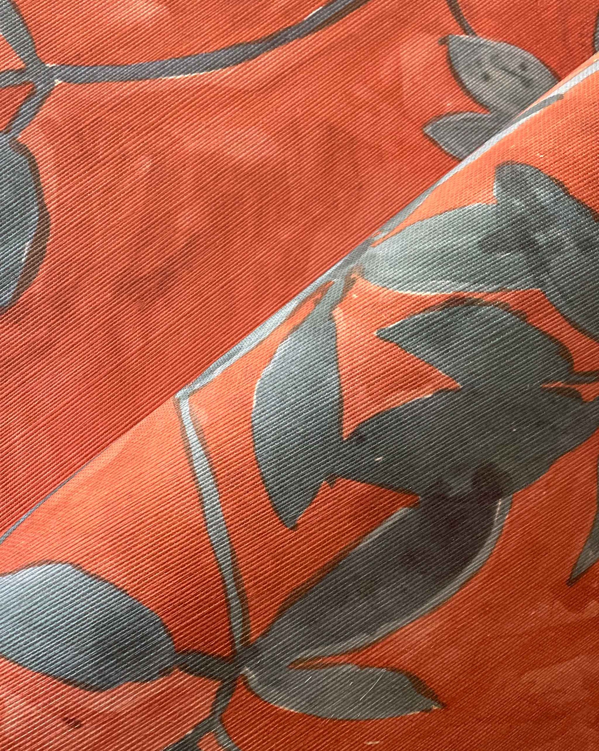 Close-up of Custom Grasscloth in orange, featuring a folded seam and a gray-green leaf pattern. The texture and weave are clearly visible, reminiscent of high-end custom designs.