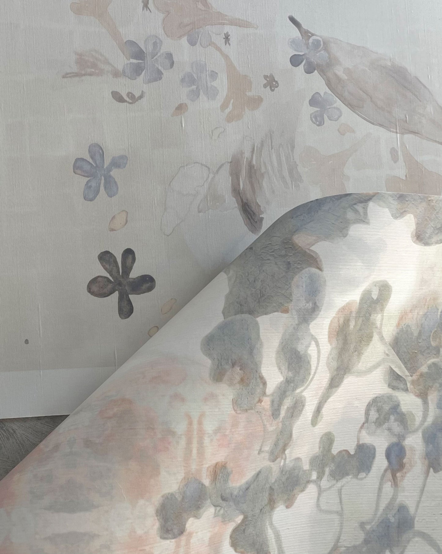 A close-up of wallpaper being peeled back to reveal Custom Silk Wallcovering featuring floral and abstract patterns in soft pastel colors underneath.