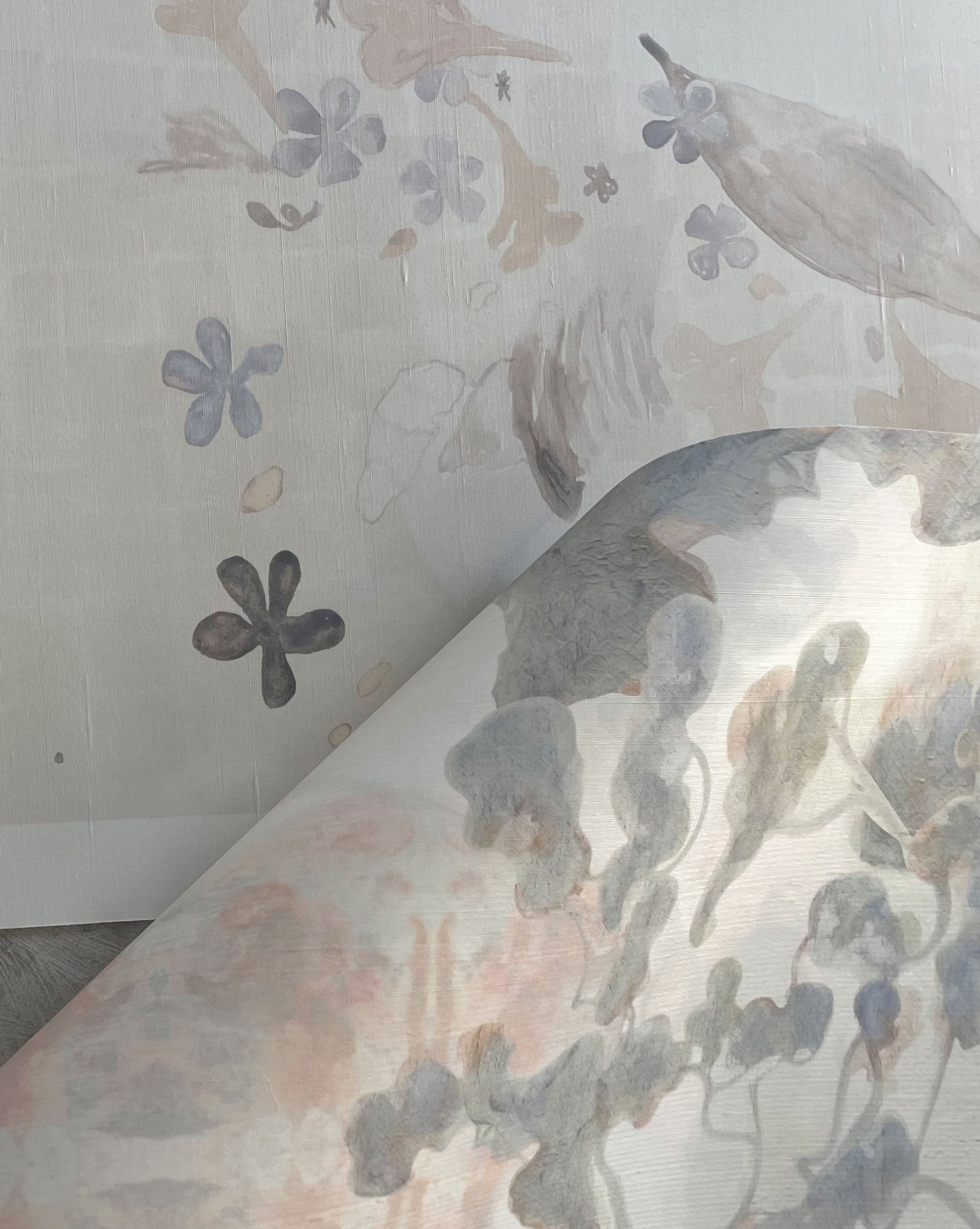 A close-up of wallpaper being peeled back to reveal Custom Silk Wallcovering featuring floral and abstract patterns in soft pastel colors underneath.