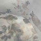 A close-up of Custom Silk Wallcovering shows semi-transparent fabric with a soft pastel floral and bird pattern, layered for depth and subtle muted colors.
