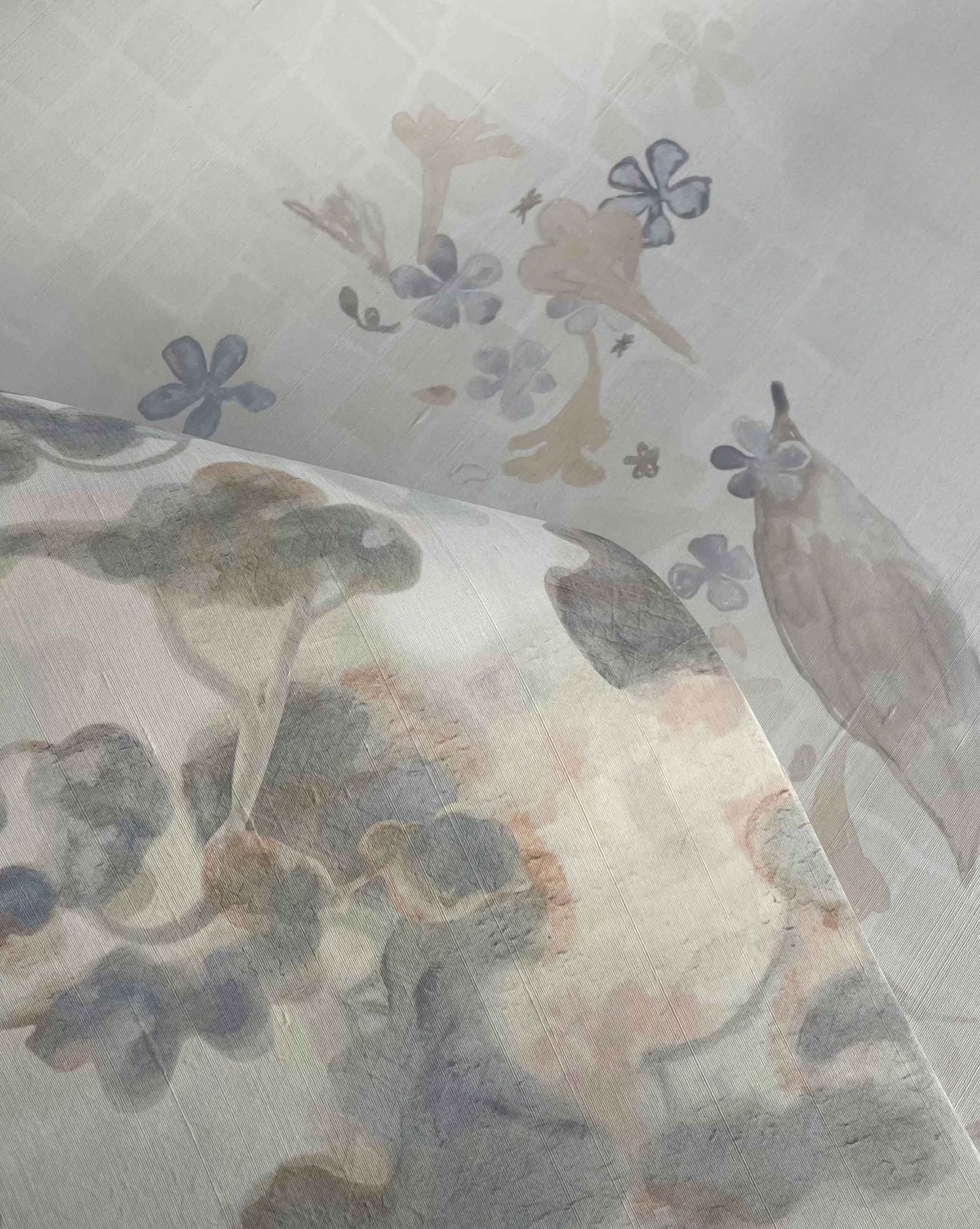 A close-up of Custom Silk Wallcovering shows semi-transparent fabric with a soft pastel floral and bird pattern, layered for depth and subtle muted colors.