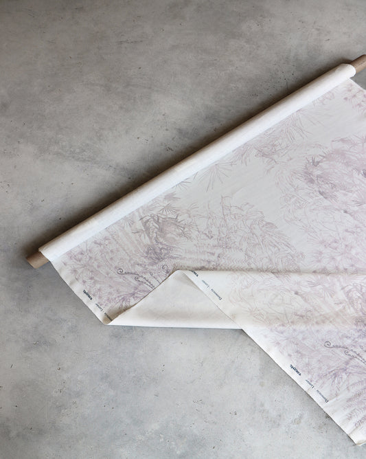 A partially unrolled roll of Domenica Fabric ||Lumier, measuring 54" wide and featuring a subtle, detailed design in Oyster Linen, is shown on a concrete floor.