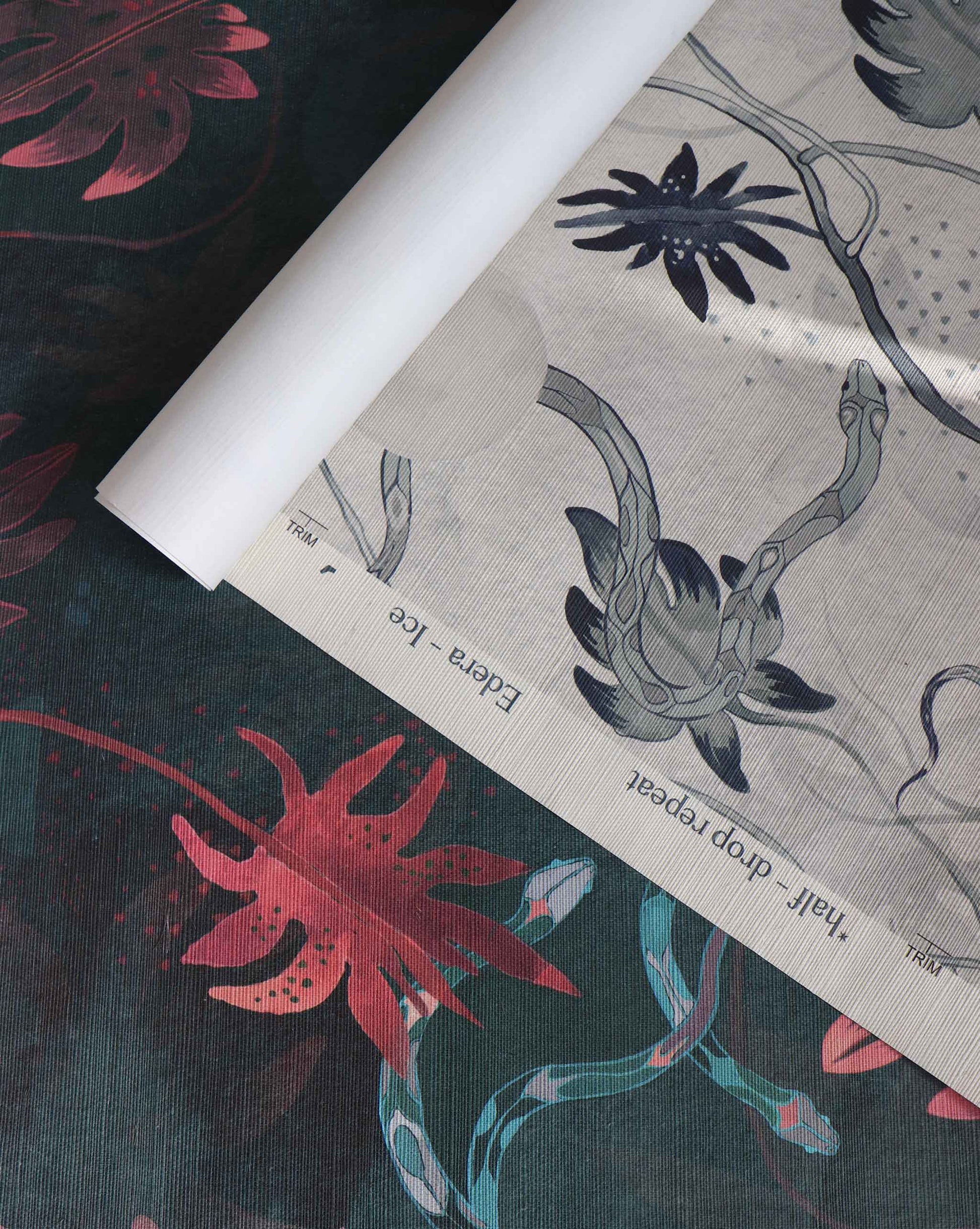 A roll of Custom Grasscloth wallpaper with a botanical pattern is partially unrolled, displaying unique designs in both color and grayscale.