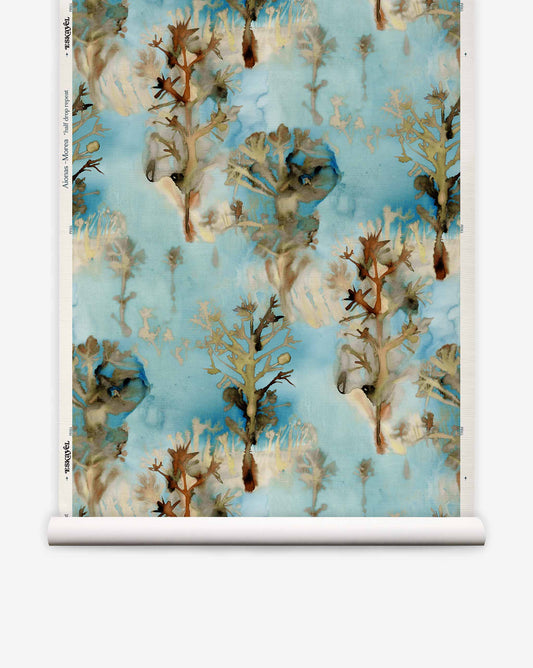 Aionas Grasscloth||Morea wallpaper roll featuring a repeating watercolor-style pattern of brown, stylized trees on a mottled blue, earthy palette background with organic shapes.