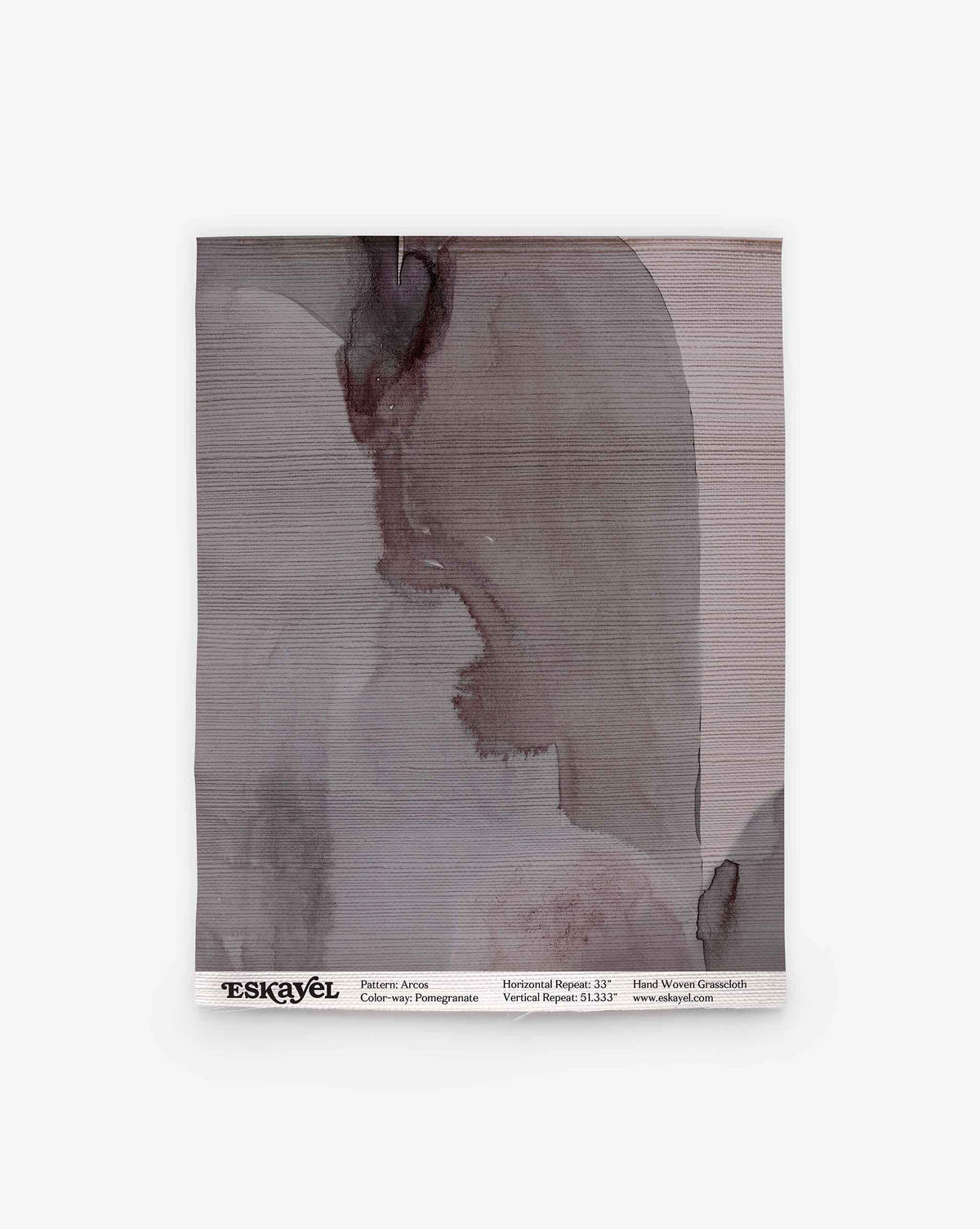 A square sample of Arcos Grasscloth||Pomegranate features abstract, muted gray and mauve watercolor patterns, evoking the subtle elegance of hand-painted wallpaper. Text at the bottom presents pattern details and branding, showcasing the nature-inspired design of this wallpaper.