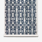 A roll of Biami Grasscloth||Nila wallpaper featuring a geometric, symmetrical navy blue on white pattern with a tie-dye effect reminiscent of woven textiles.