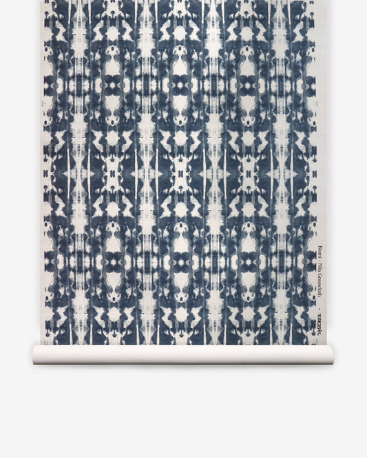 A roll of Biami Grasscloth||Nila wallpaper featuring a geometric, symmetrical navy blue on white pattern with a tie-dye effect reminiscent of woven textiles.
