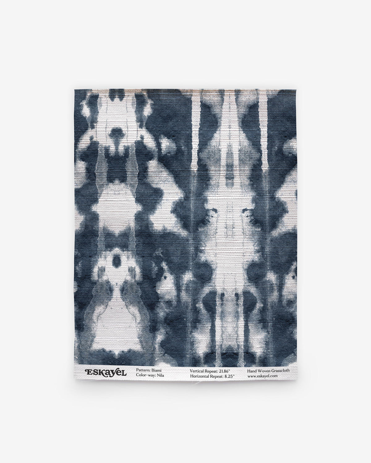 Rectangular fabric sample featuring a symmetrical indigo and white tie-dye pattern, reminiscent of blue-on-white woven textiles. Text at the bottom displays the brand name Eskayel along with details about the pattern, color (Biami Grasscloth||Nila), and website information.