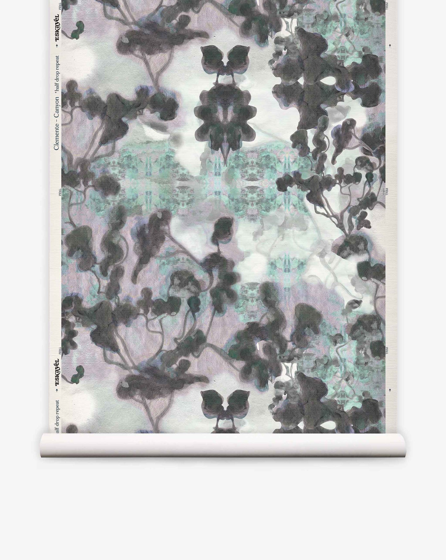 A roll of Clemente Grasscloth in the Canyon colorway from the Presidio Collection, featuring a symmetrical, abstract pattern in black, gray, and hints of blue that evokes ink blots and abstracted trees on a white background—perfect for making a unique statement with custom grasscloth wallpaper.