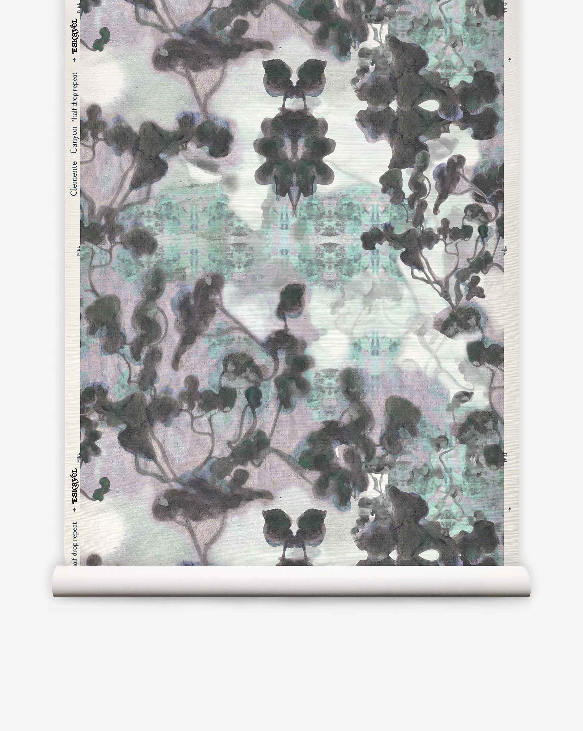 A roll of Clemente Grasscloth in the Canyon colorway from the Presidio Collection, featuring a symmetrical, abstract pattern in black, gray, and hints of blue that evokes ink blots and abstracted trees on a white background—perfect for making a unique statement with custom grasscloth wallpaper.