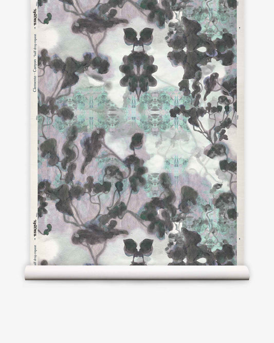 A roll of Clemente Grasscloth in the Canyon colorway from the Presidio Collection, featuring a symmetrical, abstract pattern in black, gray, and hints of blue that evokes ink blots and abstracted trees on a white background—perfect for making a unique statement with custom grasscloth wallpaper.
