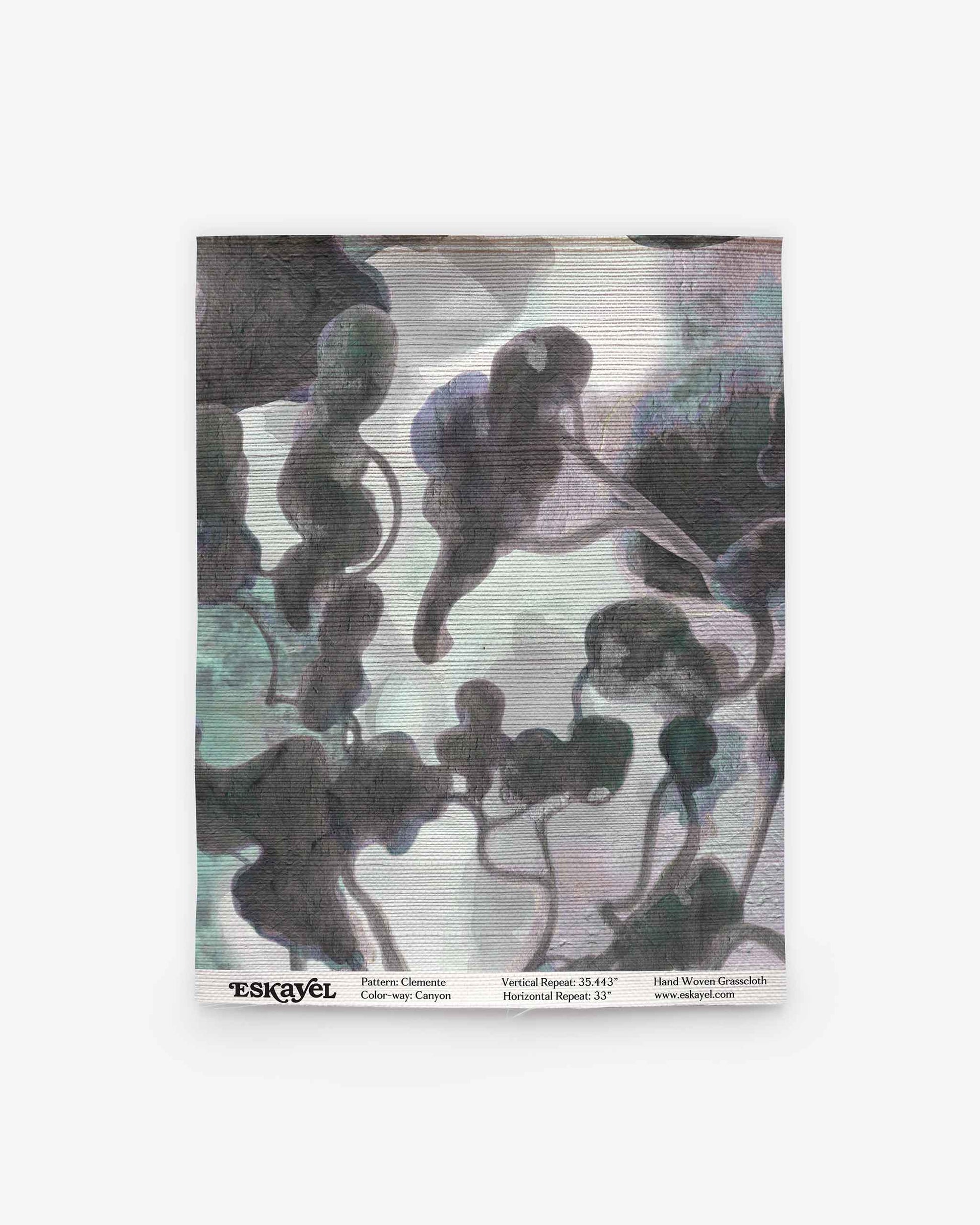 A square fabric swatch features an abstract, cloud-like watercolor pattern in muted gray, green, and purple tones on a light background, evoking the refined style of the Clemente Grasscloth||Canyon collection. Subtle text details and logo appear along the bottom edge, highlighting its inspiration from custom grasscloth wallpaper designs with abstracted tree motifs.