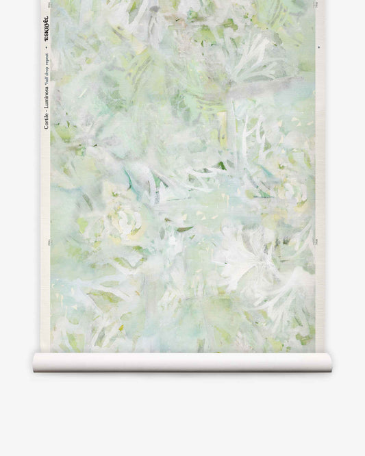 A partially unrolled roll of Cortile Grasscloth||Luminosa wallpaper, featuring a pastel green and white abstract floral design reminiscent of delicate watercolor, displayed against a white background.