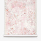 A roll of Cortile Grasscloth||Pelle wallpaper featuring a soft pink and white abstract floral design, reminiscent of watercolor patterns, is partially unrolled and displayed against a white background.
