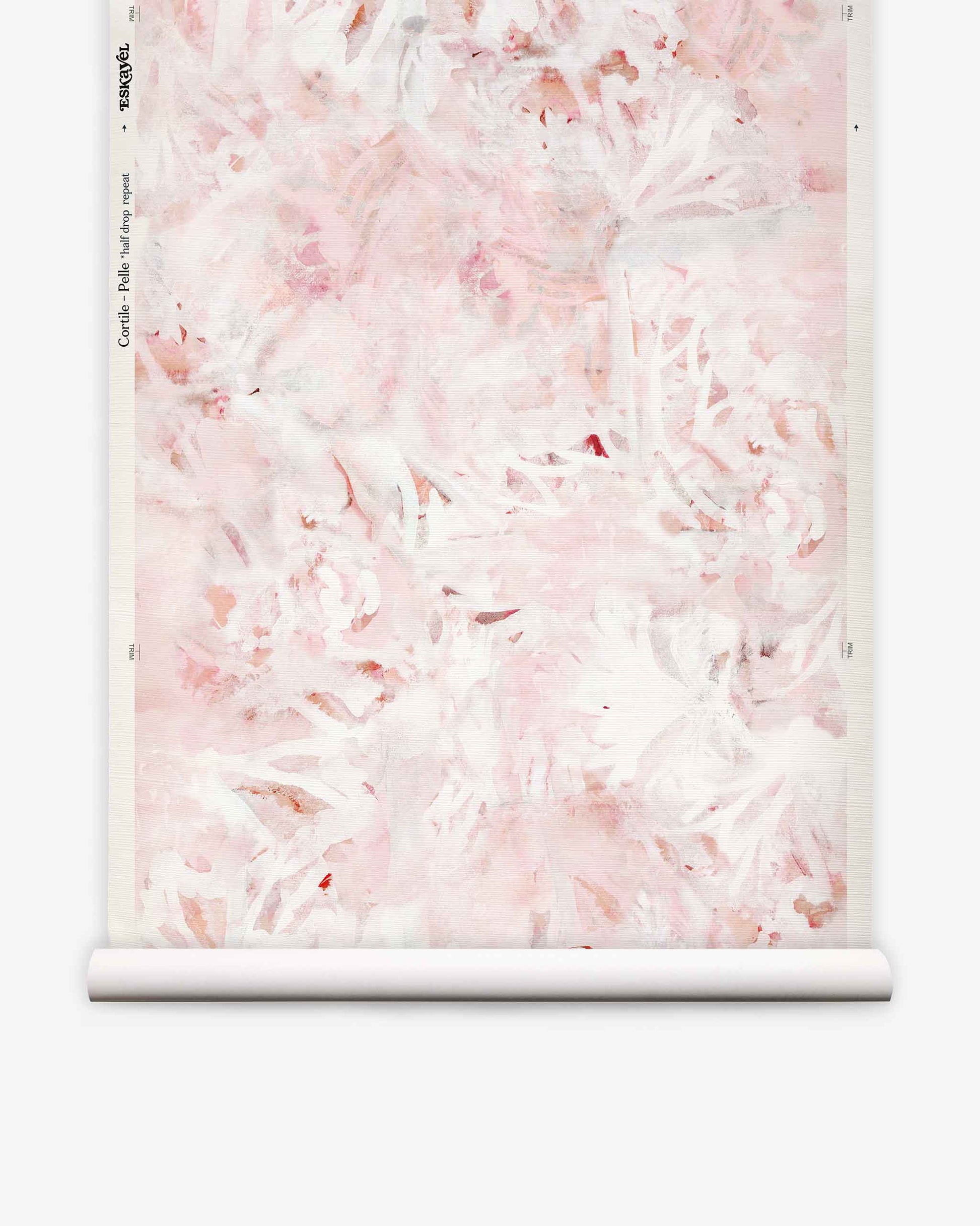 A roll of Cortile Grasscloth||Pelle wallpaper featuring a soft pink and white abstract floral design, reminiscent of watercolor patterns, is partially unrolled and displayed against a white background.