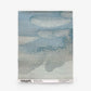 A square swatch of non-woven material featuring a blue and gray cloud-like pattern, labeled “Empyrean Grasscloth Sample||Cyrrus” at the bottom. Order a sample to experience its unique texture and design firsthand.