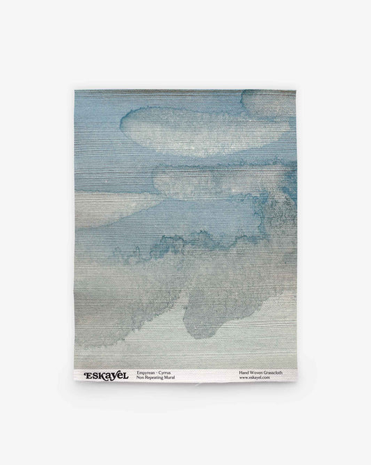 A square swatch of non-woven material featuring a blue and gray cloud-like pattern, labeled “Empyrean Grasscloth Sample||Cyrrus” at the bottom. Order a sample to experience its unique texture and design firsthand.