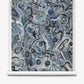 Floripa Grasscloth||Nuit features abstract artwork with swirling blue, gray, and black shapes and lines on a rolled canvas. The chaotic, organic patterns evoke doodles or graffiti, capturing the vibrant spirit of artist collaboration inspired by the dynamic culture of Florianopolis, Brazil.