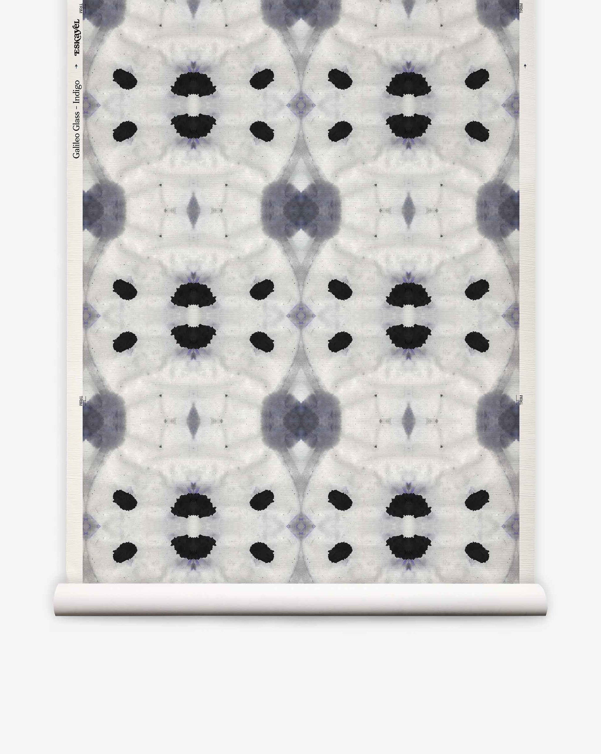 Galileo Glass Grasscloth||Indigo features an abstract black and gray symmetrical pattern reminiscent of ink blots, repeated across a white textured background with a visible paper roll edge. This exquisite wallpaper evokes the refined aesthetic of luxurious grasscloth, lending sophisticated texture and visual intrigue to any interior.