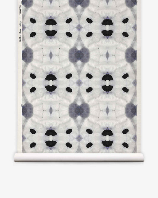 Galileo Glass Grasscloth||Indigo features an abstract black and gray symmetrical pattern reminiscent of ink blots, repeated across a white textured background with a visible paper roll edge. This exquisite wallpaper evokes the refined aesthetic of luxurious grasscloth, lending sophisticated texture and visual intrigue to any interior.