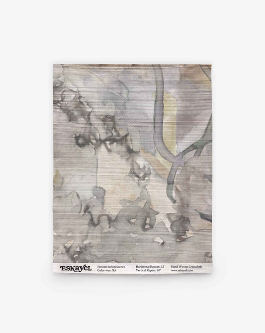 A square swatch of handwoven fabric with a gray and beige abstract watercolor pattern, labeled “Inflorescence Grasscloth||Sol” with product details at the bottom.
