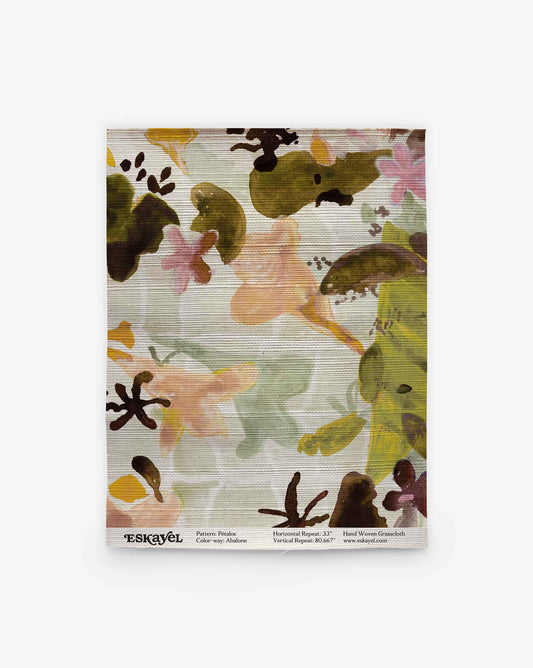A rectangular fabric swatch featuring the Pétalos Grasscloth||Abalone design, showcases an abstract ink-wash pattern in green, orange, brown, and pink hues. Pattern details and the brand name “ESKAYEL” are printed along the bottom edge.