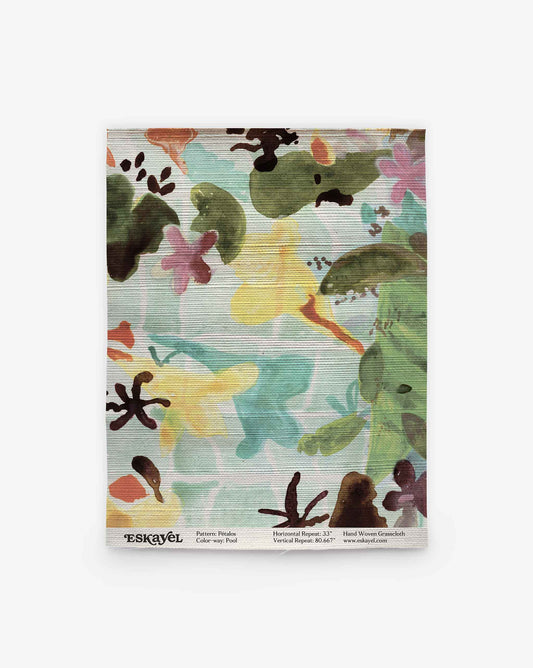 A rectangular cloth featuring the Pétalos Grasscloth||Pool design, showcasing a colorful, abstract floral pattern with green, yellow, pink, and black shapes reminiscent of hand-painted wallpaper. Text at the bottom displays brand and sizing information.