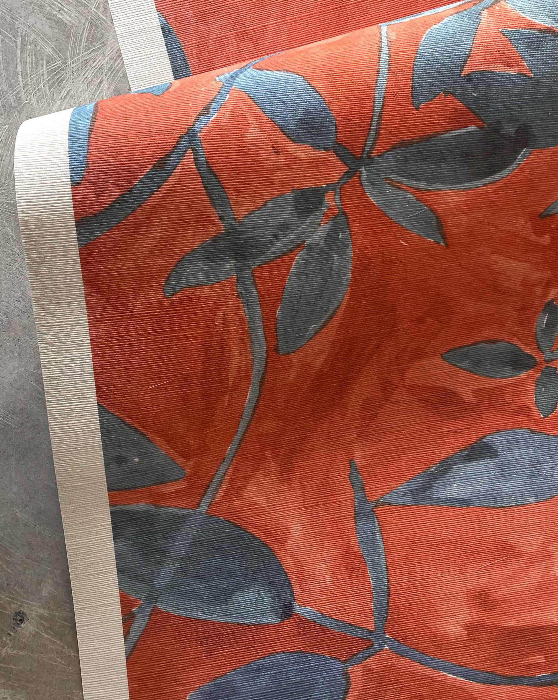 A detail photo of Eskayel’s Plumeria Shadows grasscloth wallpaper pattern in Hibiscus, a colorway with a rich red background.