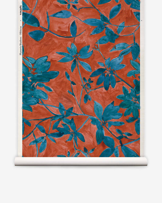 A roll of Eskayel’s Plumeria Shadows wallpaper pattern in Hibiscus, a colorway featuring a rich red background.